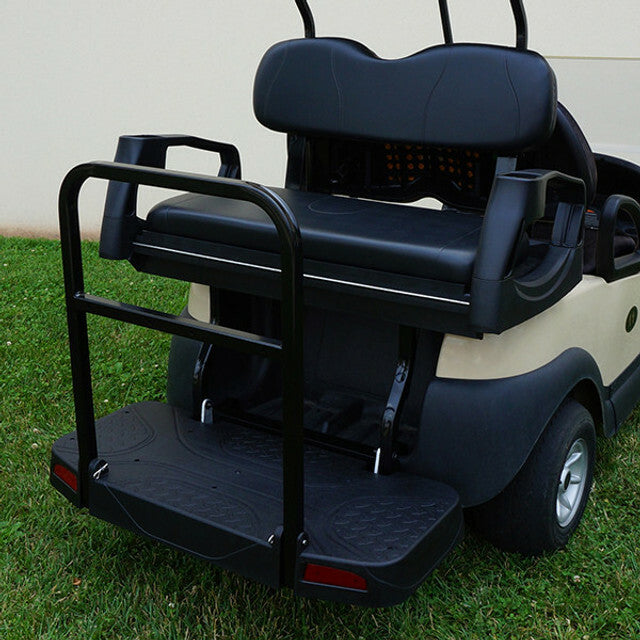Black Club Car Precedent rear flip seat kit with safety grab bar and textured cargo platform, installed on a beige golf cart parked on grass.
